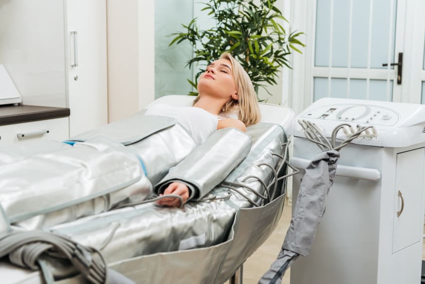 Blonde girl lying with closed eyes during pressotherapy session in clinic Pressothérapie paris 13
