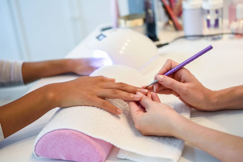 Close-up of beautician painting a woman's nails with a brush in Close-up of beautician painting a woman's nails with a brush in a nail salon. Costumer receiving a manicure.